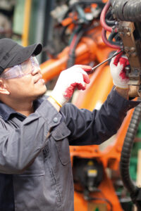 Ein Industriemechaniker in Schutzkleidung und mit Schutzbrille schraubt eine Schlauchklemme um den Hydraulikschlauch fest.